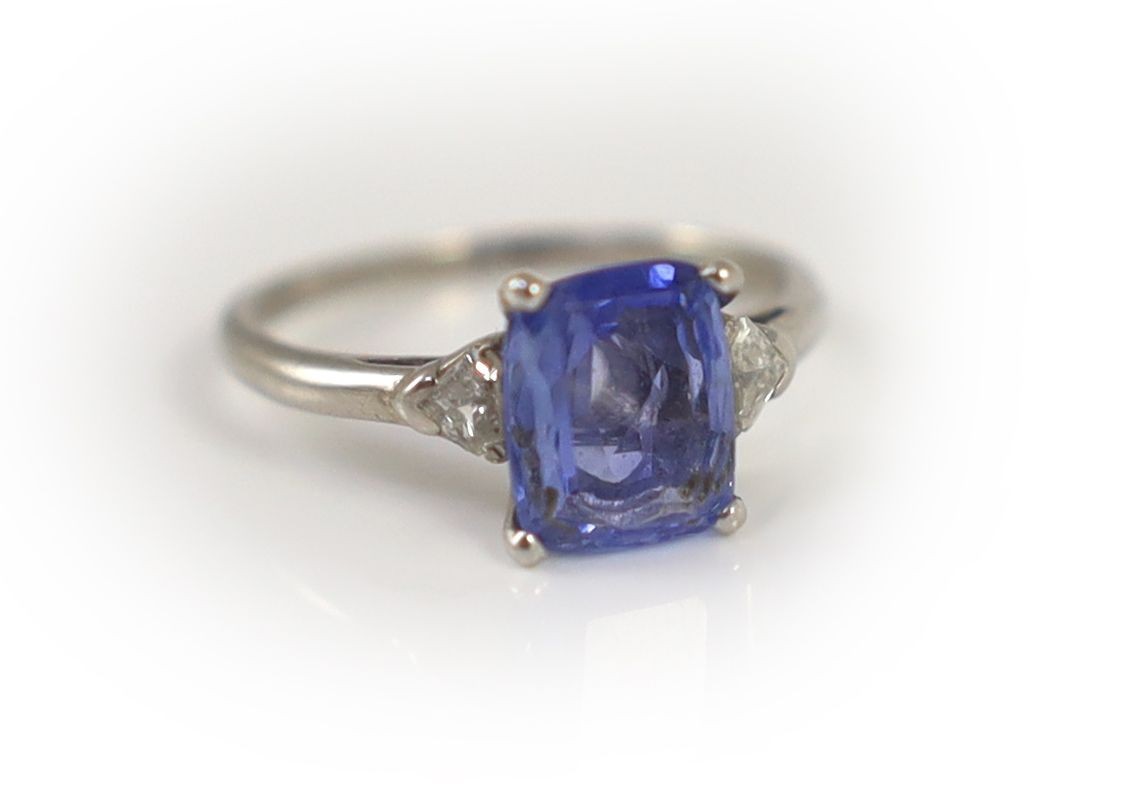 A platinum and palladium set single stone cushion cut sapphire ring, with triangular cut diamond set shoulders